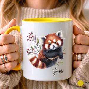 Puede incluir: Una taza de cer&aacute;mica blanca con un borde amarillo, que presenta una ilustraci&oacute;n de acuarela de un panda rojo sosteniendo una rama. La taza tiene el nombre "Jess" escrito en la parte inferior.