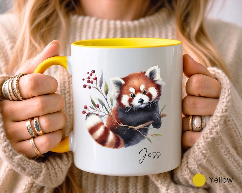 Puede incluir: Una taza de cer&aacute;mica blanca con un borde amarillo, que presenta una ilustraci&oacute;n de acuarela de un panda rojo sosteniendo una rama. La taza tiene el nombre "Jess" escrito en la parte inferior.