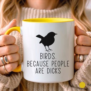 Pode incluir: Caneca de cer&acirc;mica branca com interior e al&ccedil;a amarelos. A caneca apresenta uma silhueta preta de um p&aacute;ssaro e o texto "BIRDS. BECAUSE PEOPLE ARE DICKS" em preto, com um ponto amarelo indicando a cor.