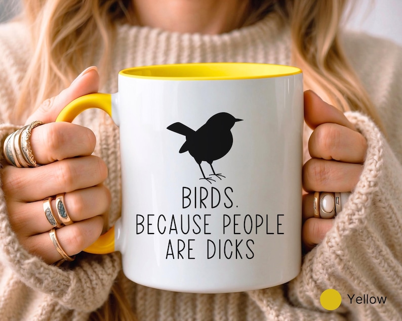 Pode incluir: Caneca de cer&acirc;mica branca com interior e al&ccedil;a amarelos. A caneca apresenta uma silhueta preta de um p&aacute;ssaro e o texto "BIRDS. BECAUSE PEOPLE ARE DICKS" em preto, com um ponto amarelo indicando a cor.