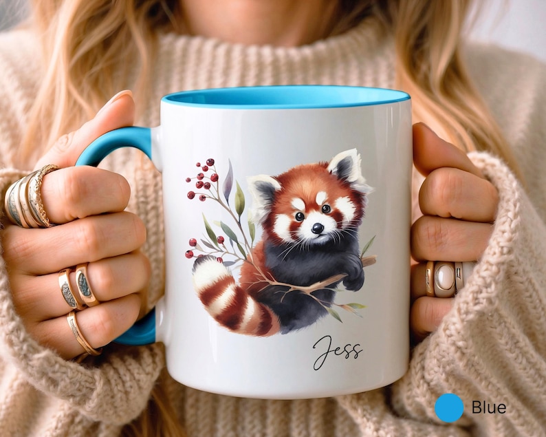 Puede incluir: Taza de cer&aacute;mica blanca con borde y asa azules. La taza presenta una ilustraci&oacute;n de acuarela de un panda rojo sosteniendo una rama con bayas. El nombre "Jess" est&aacute; escrito en cursiva en la parte inferior de la taza.
