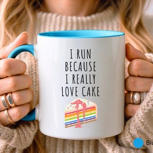 May include: White ceramic mug with a blue rim. The mug has a black text that reads "I run because I really love cake" and a colorful cake slice illustration.