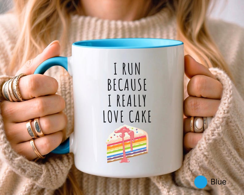 May include: White ceramic mug with a blue rim. The mug has a black text that reads "I run because I really love cake" and a colorful cake slice illustration.