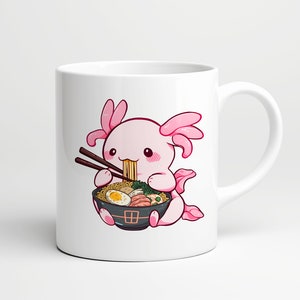 May include: A white ceramic mug featuring a colourful illustration of a pink axolotl eating a bowl of ramen with dark brown chopsticks. The ramen bowl is black with a small red square design and contains noodles, a halved boiled egg, and greens.