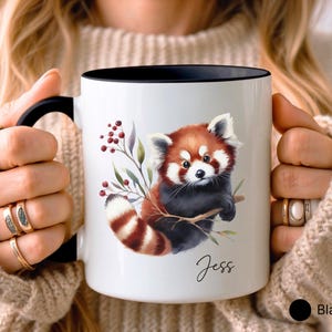 Puede incluir: Taza de cer&aacute;mica blanca con borde y asa negros. La taza presenta una ilustraci&oacute;n de acuarela de un panda rojo sujetando una rama con bayas y hojas. El nombre "Jess" est&aacute; escrito en cursiva en la parte inferior de la taza.