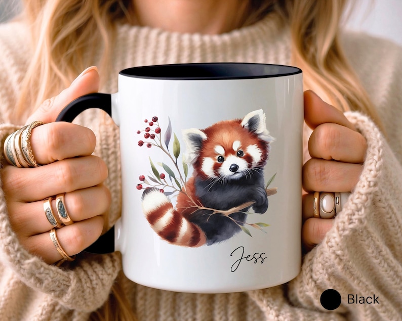 Puede incluir: Taza de cer&aacute;mica blanca con borde y asa negros. La taza presenta una ilustraci&oacute;n de acuarela de un panda rojo sujetando una rama con bayas y hojas. El nombre "Jess" est&aacute; escrito en cursiva en la parte inferior de la taza.