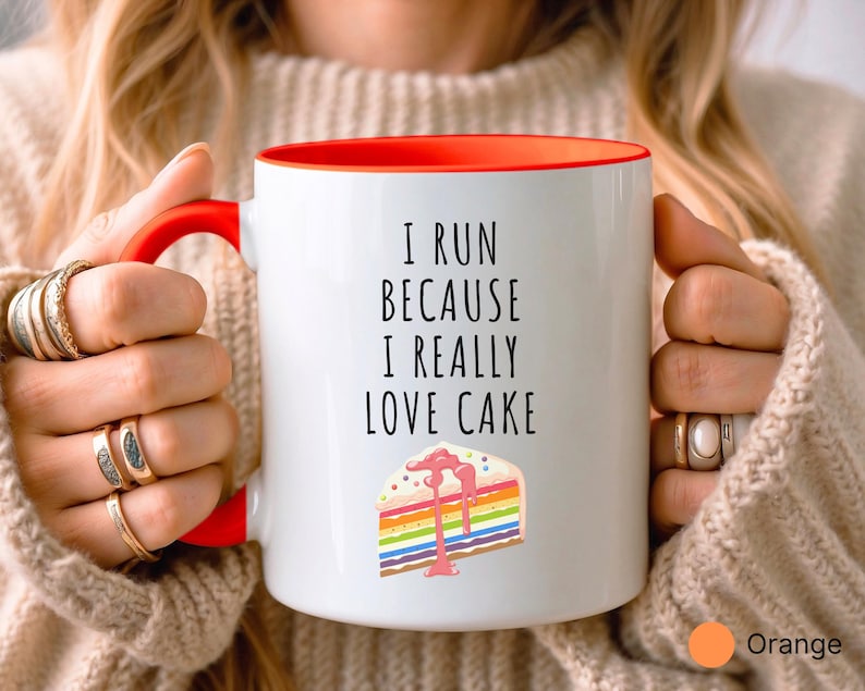May include: White coffee mug with an orange rim. The mug has a black inscription that reads "I run because I really love cake". A colorful cake slice with rainbow frosting is pictured below the text.