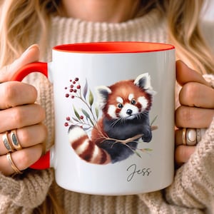 Puede incluir: Taza de cer&aacute;mica blanca con borde rojo, con una ilustraci&oacute;n de acuarela de un panda rojo sosteniendo una rama con bayas. La taza tiene el nombre "Jess" escrito en cursiva en la parte inferior.