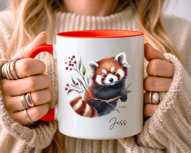 Puede incluir: Taza de cer&aacute;mica blanca con borde rojo, con una ilustraci&oacute;n de acuarela de un panda rojo sosteniendo una rama con bayas. La taza tiene el nombre "Jess" escrito en cursiva en la parte inferior.