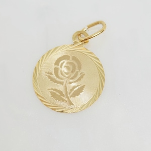May include: A round gold pendant featuring an engraved rose design in the center. The surface of the pendant has a textured finish with a diagonal line pattern along the outer edge. A small gold jump ring is attached to the top of the circular charm.