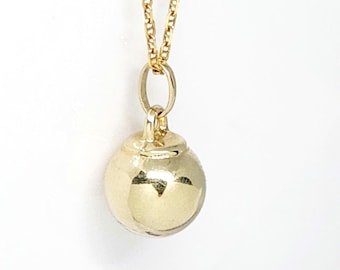 May include: A gold necklace featuring a polished, spherical charm pendant suspended from a delicate gold chain. The smooth, round ball pendant is attached to the chain by a small, circular jump ring, creating a simple and reflective metallic design.