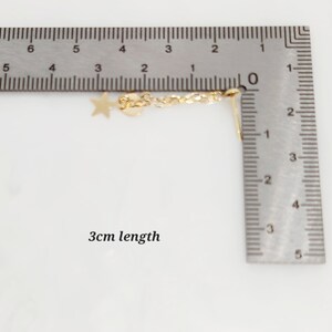May include: A gold chain with a star and heart charm, measuring 3 cm in length. The chain is shown next to a ruler for size reference.