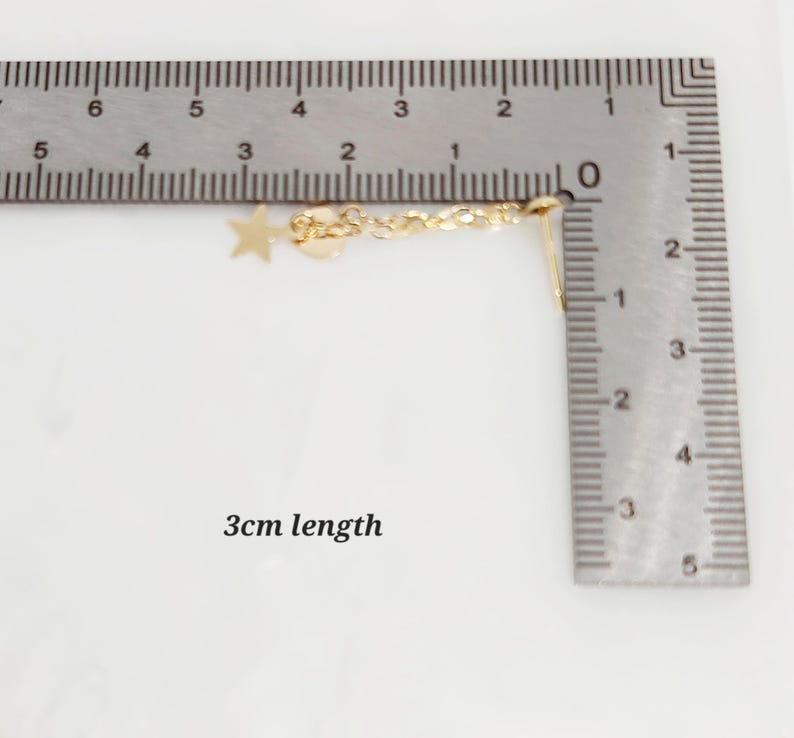May include: A gold chain with a star and heart charm, measuring 3 cm in length. The chain is shown next to a ruler for size reference.