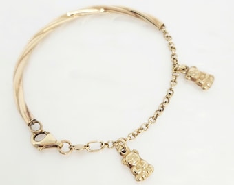 May include: A gold-toned bracelet featuring a twisted metal semi-rigid band connected to a delicate chain link section. Two small, three-dimensional gold-toned bear charms are suspended from the chain, and the bracelet secures with a lobster clasp.