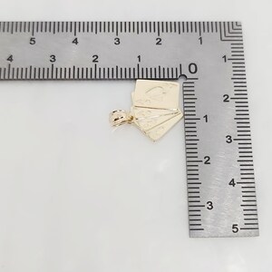 May include: A gold-colored metal pendant shaped like a fan of playing cards, featuring an ace of spades design. The pendant is positioned next to a metal ruler, showing a width of approximately 0.75 inches and a height of 0.75 inches.