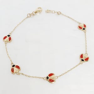 Peut inclure: Un bracelet doré orné de cinq breloques coccinelles. Chaque breloque présente des détails en émail rouge et noir. Le bracelet est doté d'une fine chaîne et d'un fermoir mousqueton.