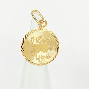 May include: A round gold pendant featuring a textured surface with two embossed hearts in the centre and the text I Love You engraved in a script font. The pendant has a decorative twisted rope-style border and a small gold jump ring at the top.