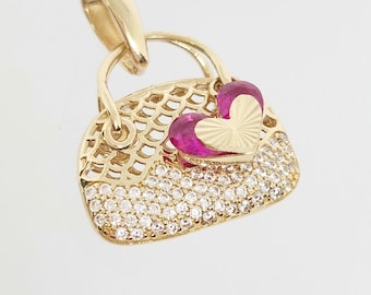 May include: A gold pendant shaped like a handbag, featuring a top section with a gold lattice pattern, a bottom section encrusted with clear stones, and a central accent consisting of a pink heart-shaped stone layered with a small gold heart.