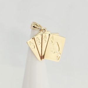 May include: A gold pendant shaped like a fan of four playing cards, each featuring an ace. The cards display the heart, club, diamond, and spade suits. The pendant includes a small gold bail at the top for attachment to a chain or necklace.