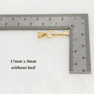 May include: A gold-colored key pendant, 0.67 inches long and 0.35 inches wide without the bail, is displayed next to a ruler. The text "17mm x 9mm without bail" is also visible.