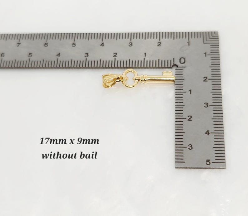 May include: A gold-colored key pendant, 0.67 inches long and 0.35 inches wide without the bail, is displayed next to a ruler. The text "17mm x 9mm without bail" is also visible.
