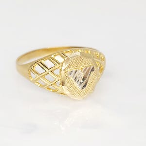 May include: A gold ring with a diamond-shaped face and a lattice design on the band. The face of the ring has a textured surface with a triangle design in the center. The ring is set against a white background.