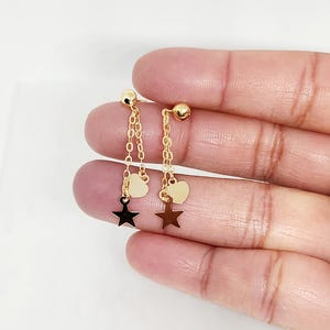 May include: A pair of gold earrings with a dangling star charm and a heart charm on each earring.