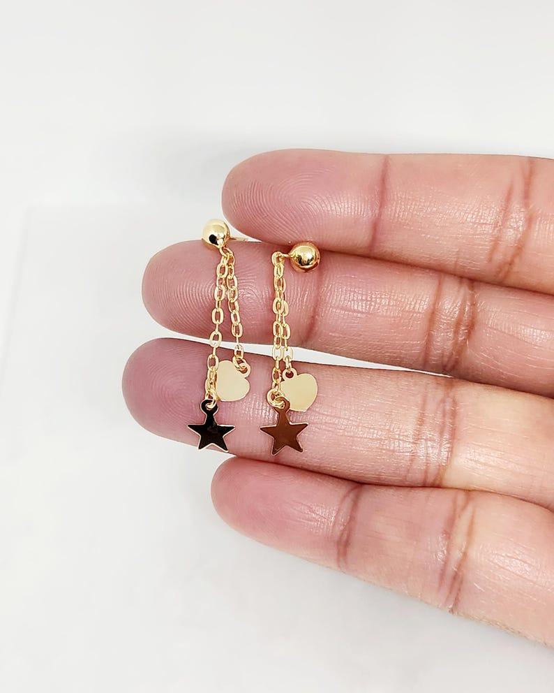 May include: A pair of gold earrings with a dangling star charm and a heart charm on each earring.