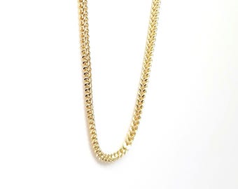 May include: A gold-toned chain necklace featuring a dense, woven wheat or franco link pattern. The metal links are tightly interconnected, creating a smooth, rounded, and continuous rope-like texture that reflects light along its entire length.