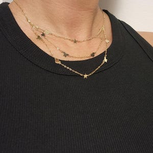 May include: A gold layered necklace with star charms. The necklace is on a model wearing a black tank top.