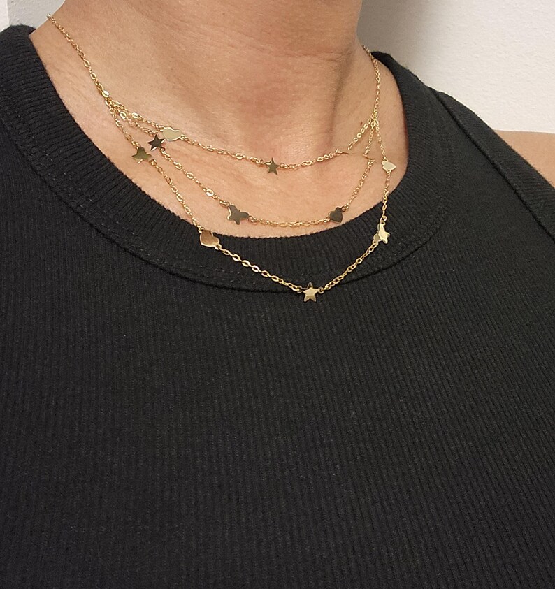 May include: A gold layered necklace with star charms. The necklace is on a model wearing a black tank top.