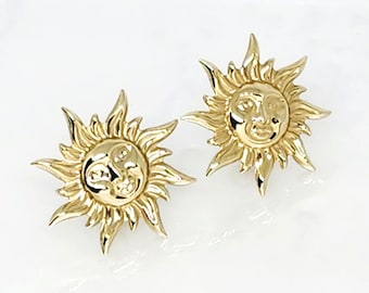Peut inclure: Une paire de boucles d'oreilles à clous dorées représentant un soleil avec un visage central et des rayons pointus rayonnants. La surface métallique présente une finition polie, créant un aspect réfléchissant sur les motifs solaires.