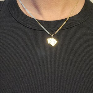 May include: A gold-toned necklace featuring a pendant shaped like a small fan of three playing cards. The pendant hangs from a delicate, thin gold-toned chain. The playing card design is metallic gold with visible engraved details on the surface.