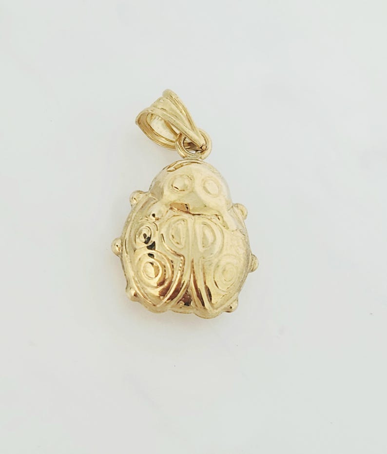 K&ouml;nnte beinhalten: Ein goldener Anh&auml;nger in Form eines Marienk&auml;fers mit polierter Oberfl&auml;che. Das Insektendesign zeigt gepr&auml;gte kreisf&ouml;rmige Muster auf den Fl&uuml;geln und einen glatten Kopfbereich. Eine kleine dreieckige &Ouml;se ist oben zur Befestigung angebracht.