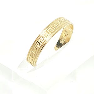 Puede incluir: Un anillo de metal color oro con un diseño de banda abierta. La superficie exterior del anillo está decorada con un patrón de greca grabado en relieve continuo. El interior de la banda muestra un sello claro que indica la pureza del metal.