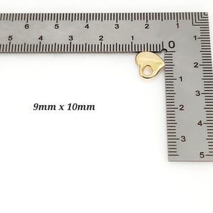 May include: A small, gold-coloured heart-shaped charm with a circular hole at the top for attachment. The charm is positioned next to a metal L-shaped ruler, with the text 9mm x 10mm printed on the side, indicating its specific physical dimensions.