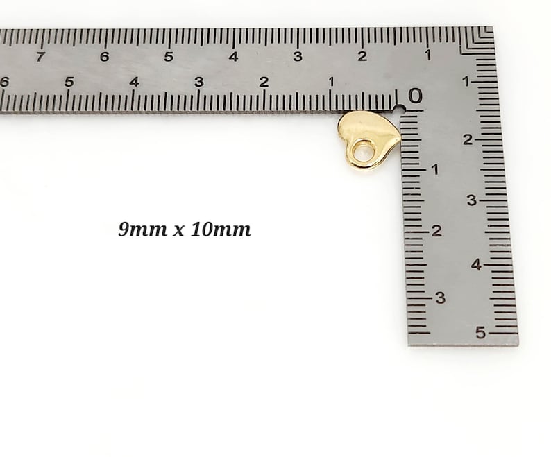 May include: A small, gold-coloured heart-shaped charm with a circular hole at the top for attachment. The charm is positioned next to a metal L-shaped ruler, with the text 9mm x 10mm printed on the side, indicating its specific physical dimensions.