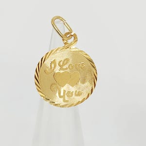 May include: A round gold pendant featuring a textured border and the engraved text I Love You with two central heart shapes. The pendant includes a small circular bail at the top for attachment to a chain, showcasing a polished finish.