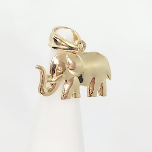 May include: A polished gold elephant pendant featuring a smooth, reflective surface and a detailed trunk, ear, and leg structure. The charm includes a sturdy, integrated gold bail at the top, designed for attachment to a necklace chain or bracelet.