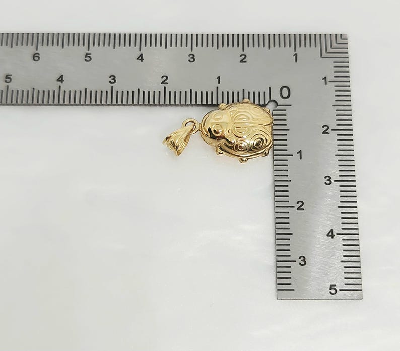 K&ouml;nnte beinhalten: Ein goldfarbener Metallanh&auml;nger in Form eines Marienk&auml;fers mit eingravierten kreisf&ouml;rmigen Mustern, der neben einem Metalllineal liegt, das zeigt, dass der Anh&auml;nger etwa 1,9 cm breit und 1,3 cm hoch ist, inklusive der &Ouml;se.