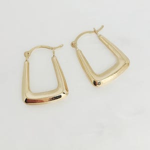 May include: A pair of gold hoop earrings with a distinct U-shaped or square-bottomed design. The earrings feature a polished, reflective metallic finish and a hinged post mechanism at the top for secure closure, showcasing a smooth, rounded profile.