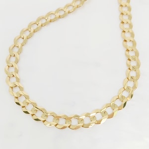 May include: A gold-colored curb chain necklace. The chain is made of interlocking oval links. The necklace is displayed on a white surface. The chain is a classic jewelry piece.