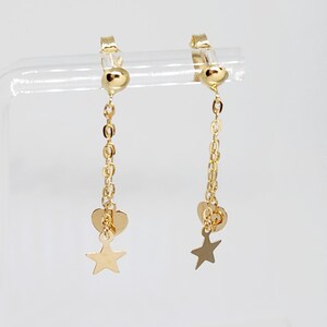 May include: A pair of gold clip-on earrings with a dangling chain, heart, and star charm.