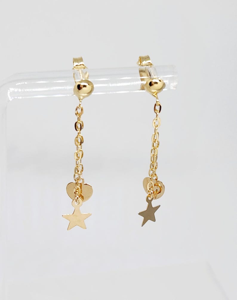 May include: A pair of gold clip-on earrings with a dangling chain, heart, and star charm.