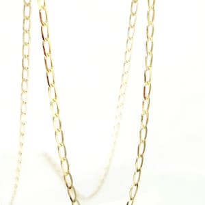 May include: A gold-toned chain necklace featuring elongated, oval-shaped links connected in a continuous series. The chain has a polished, reflective surface and hangs in a gentle, curved drape, showcasing the uniform size and shape of each individual link.