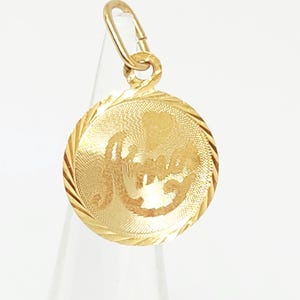May include: A round gold pendant featuring a textured surface with the word "Amor" inscribed in the center. The pendant has a decorative twisted rope-style border and includes a small gold jump ring at the top for attachment to a chain.