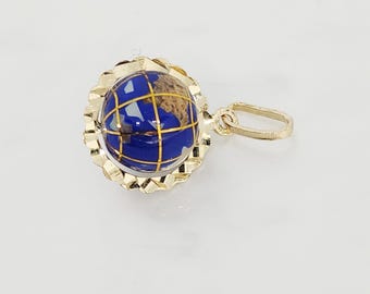 May include: A gold-colored pendant featuring a globe design. The globe has a blue enamel surface with gold-colored grid lines and landmass details. The pendant is surrounded by a scalloped gold-colored frame and has a small loop for a chain.
