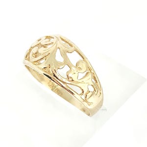 May include: A gold ring featuring an intricate openwork filigree design across the band. The metal surface is polished and reflective, showcasing a repeating scrollwork pattern. The interior of the band is clearly stamped with the text 10K EC.
