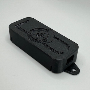 May include: A black 3D printed case with a logo of a brake rotor and calipers. The case has a small hole on the side and a loop on the bottom.