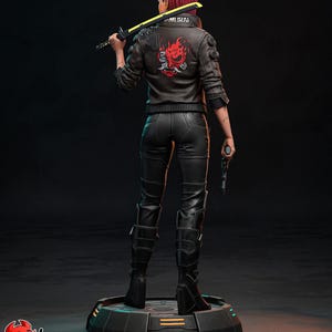 May include: A figurine of a character from Cyberpunk 2077, viewed from the back. The figure has red hair and wears a black leather jacket with a red and white design, black pants, and boots. The figure holds a yellow and black sword and a gun.